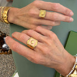 Close-up of gold ring and pink enamel ring being worn on a green surface.