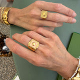Close-up of gold ring and pink enamel ring being worn on a green surface.