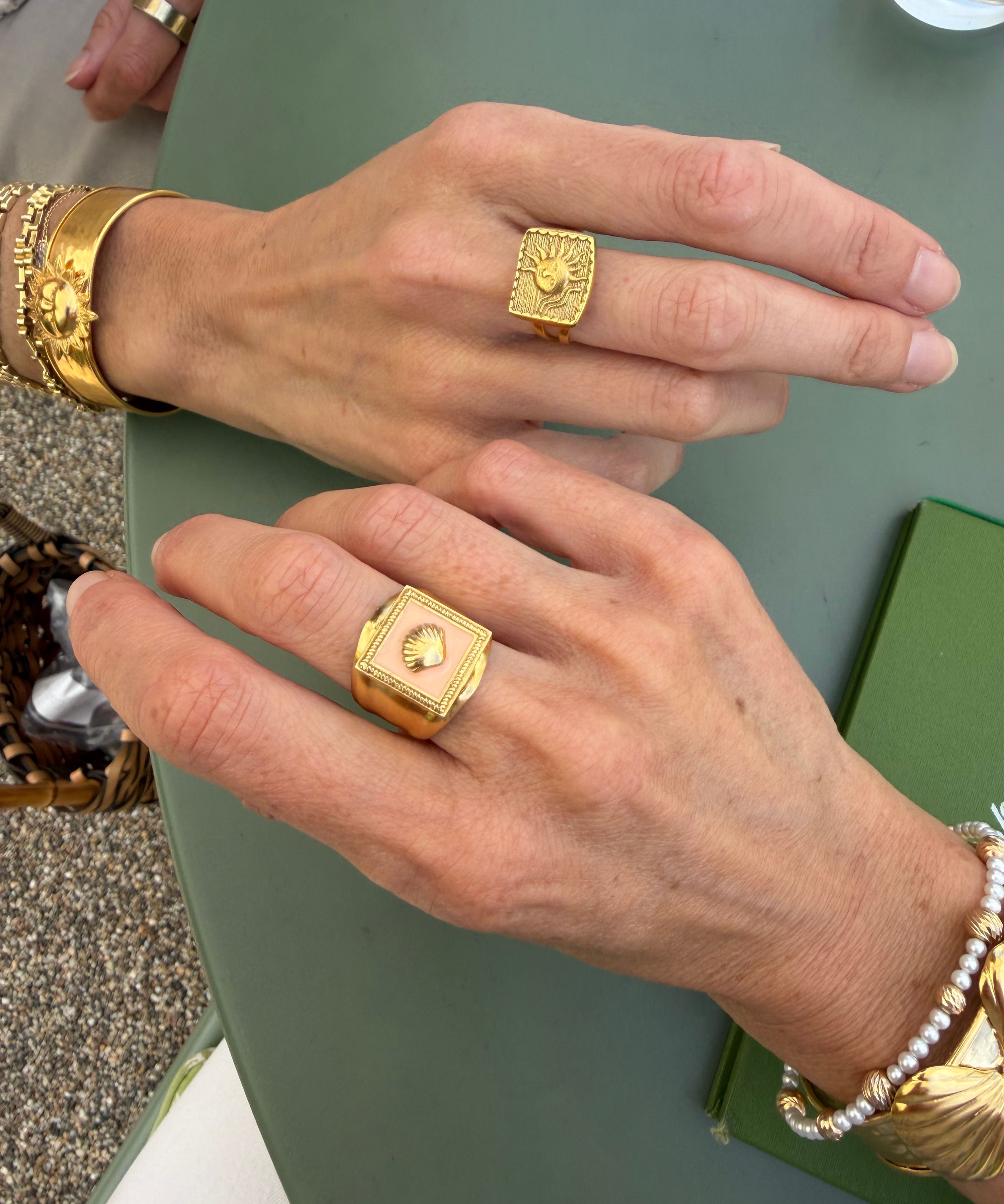 Close-up of gold ring and pink enamel ring being worn on a green surface.