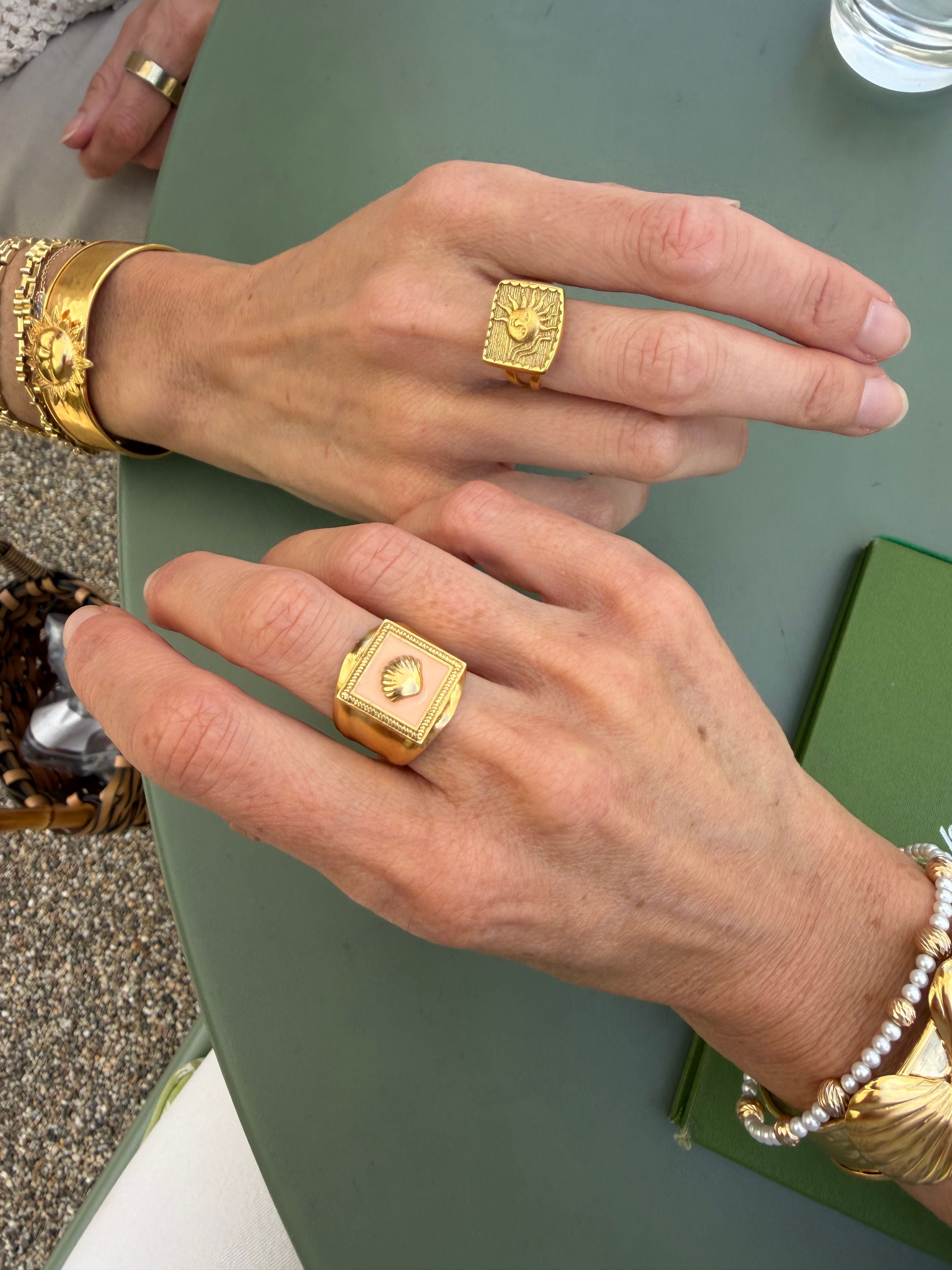 Close-up of gold ring and pink enamel ring being worn on a green surface.