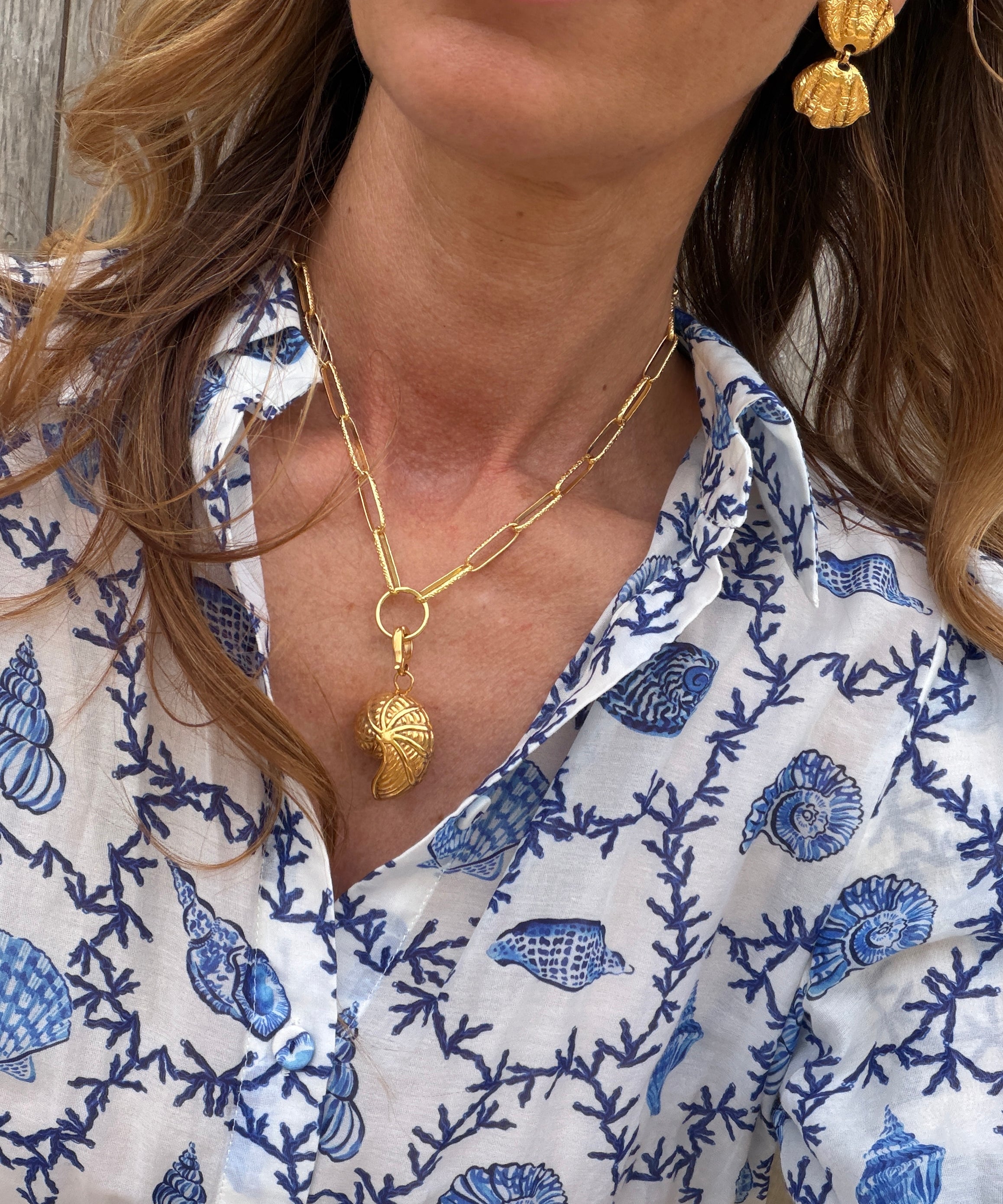 Gold coloured necklace with gold coloured shell shaped charm and earrings worn.