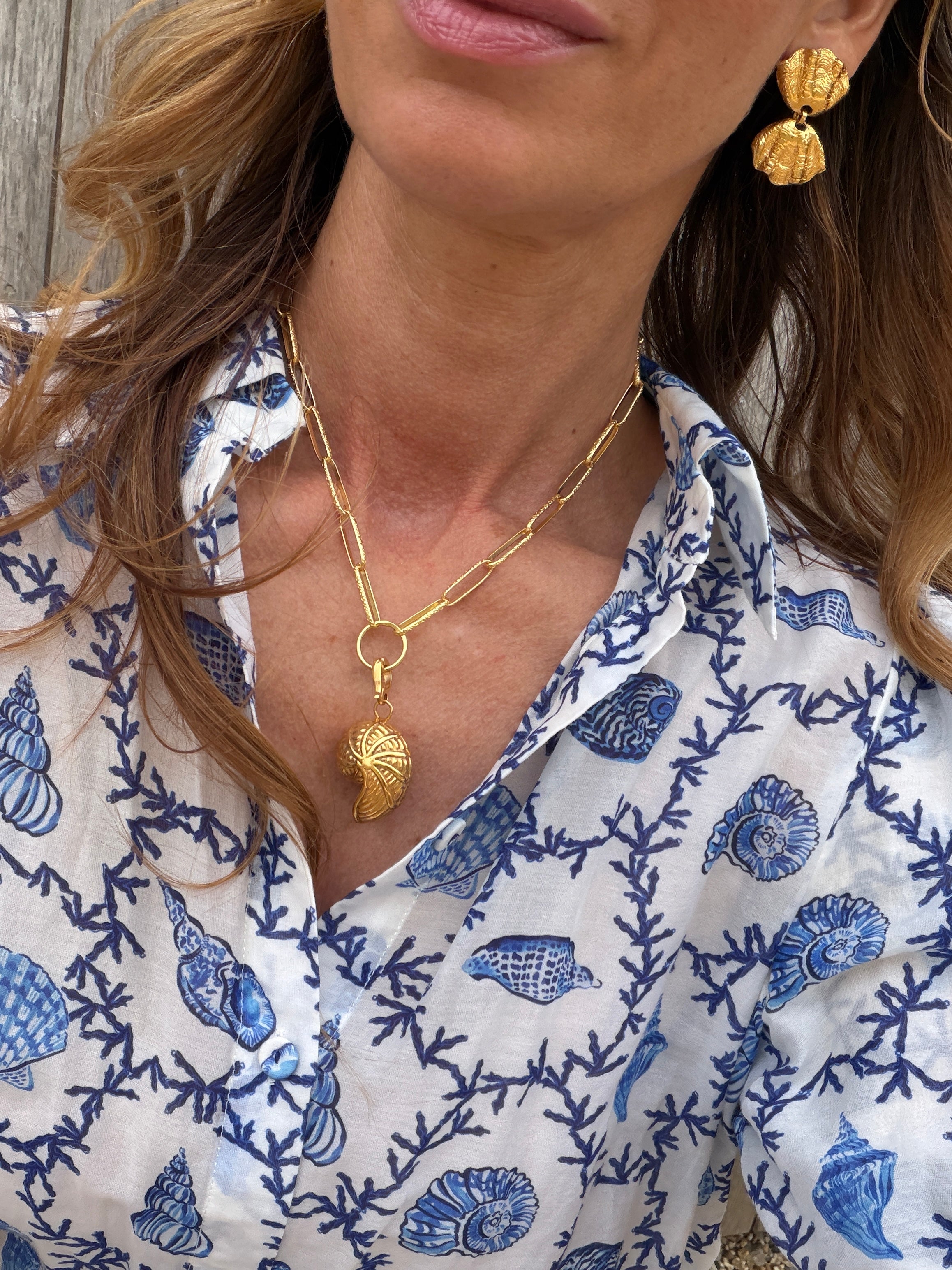 Gold coloured necklace with gold coloured shell shaped charm and earrings worn.