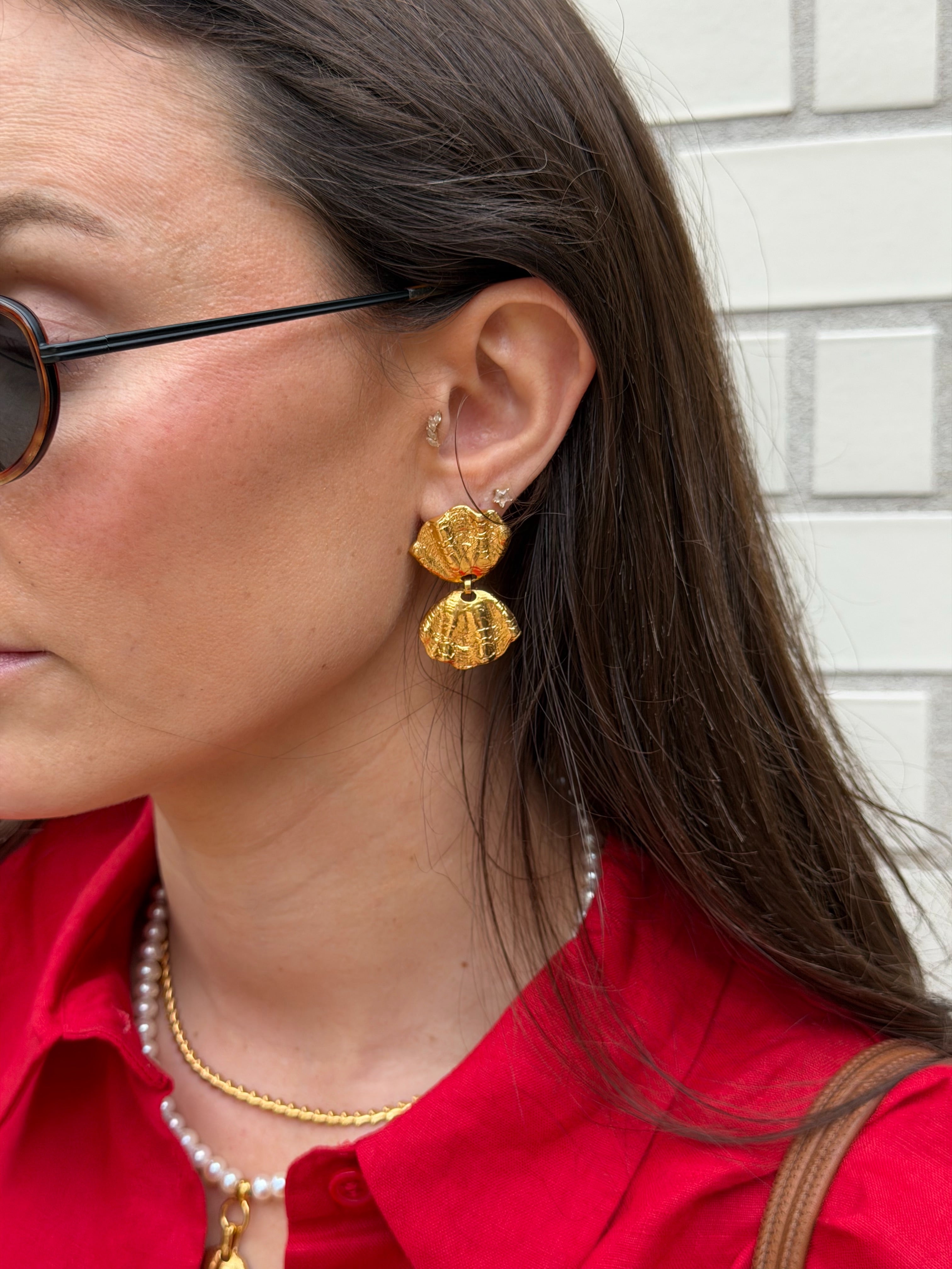 Close-up of a woman wearing gold coloured earrings with a shell design worn