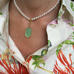 Close-up of a pearl necklace with a green pendant on a person wearing a colorful floral shirt.