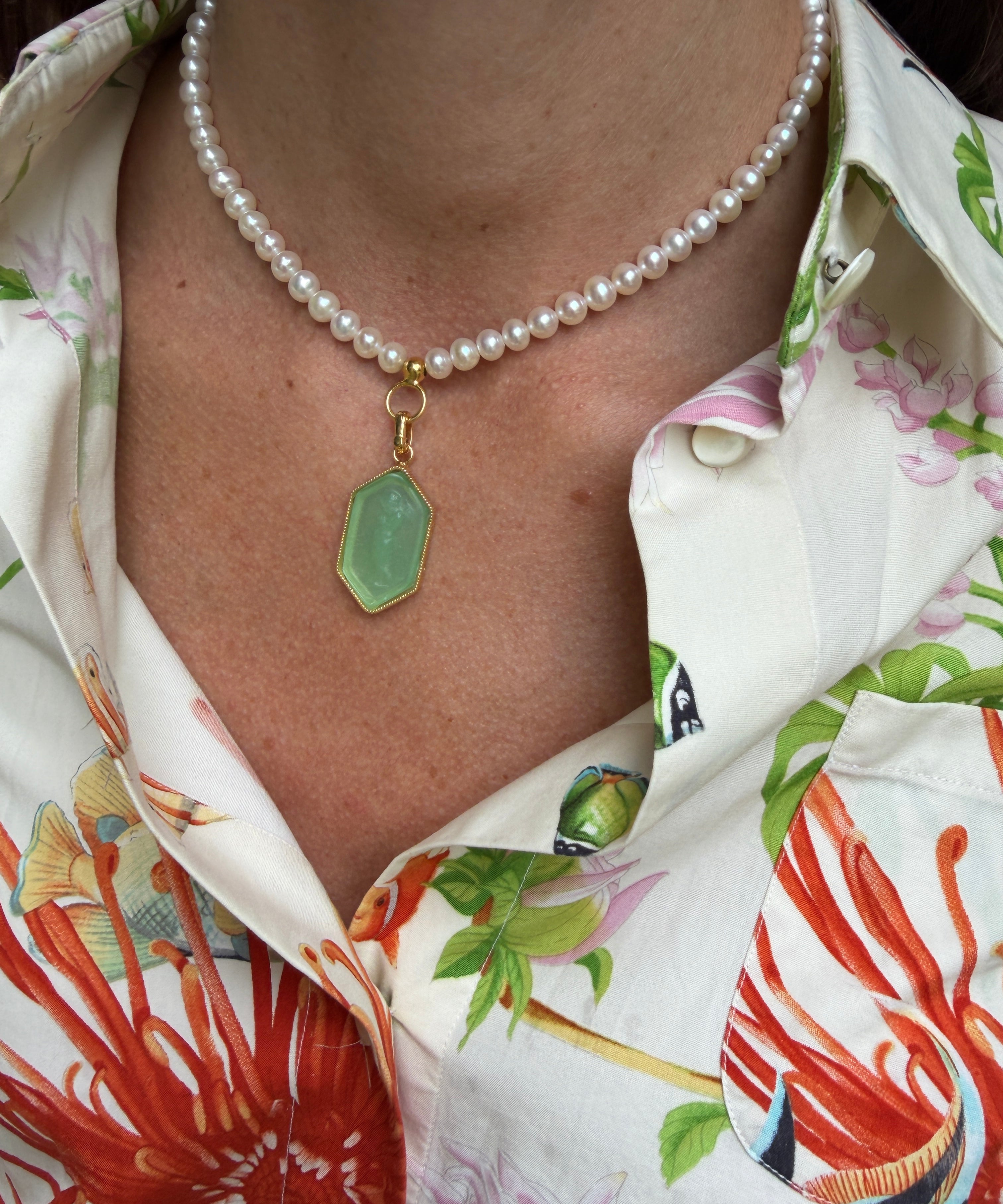 Close-up of a pearl necklace with a green pendant on a person wearing a colorful floral shirt.
