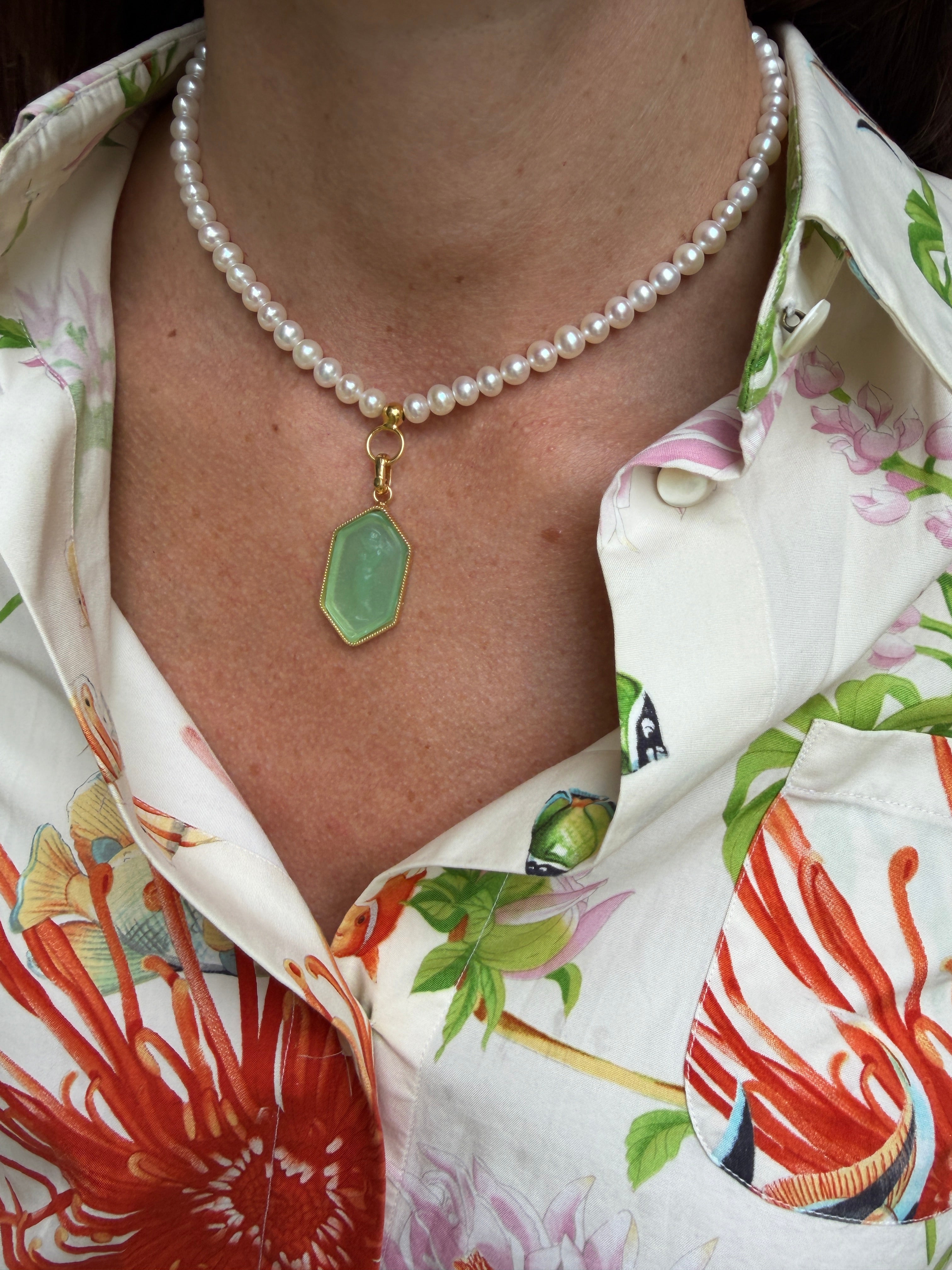 Close-up of a pearl necklace with a green pendant on a person wearing a colorful floral shirt.
