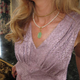 green charm on a pearl necklace a woman wearing it with a lilac dress