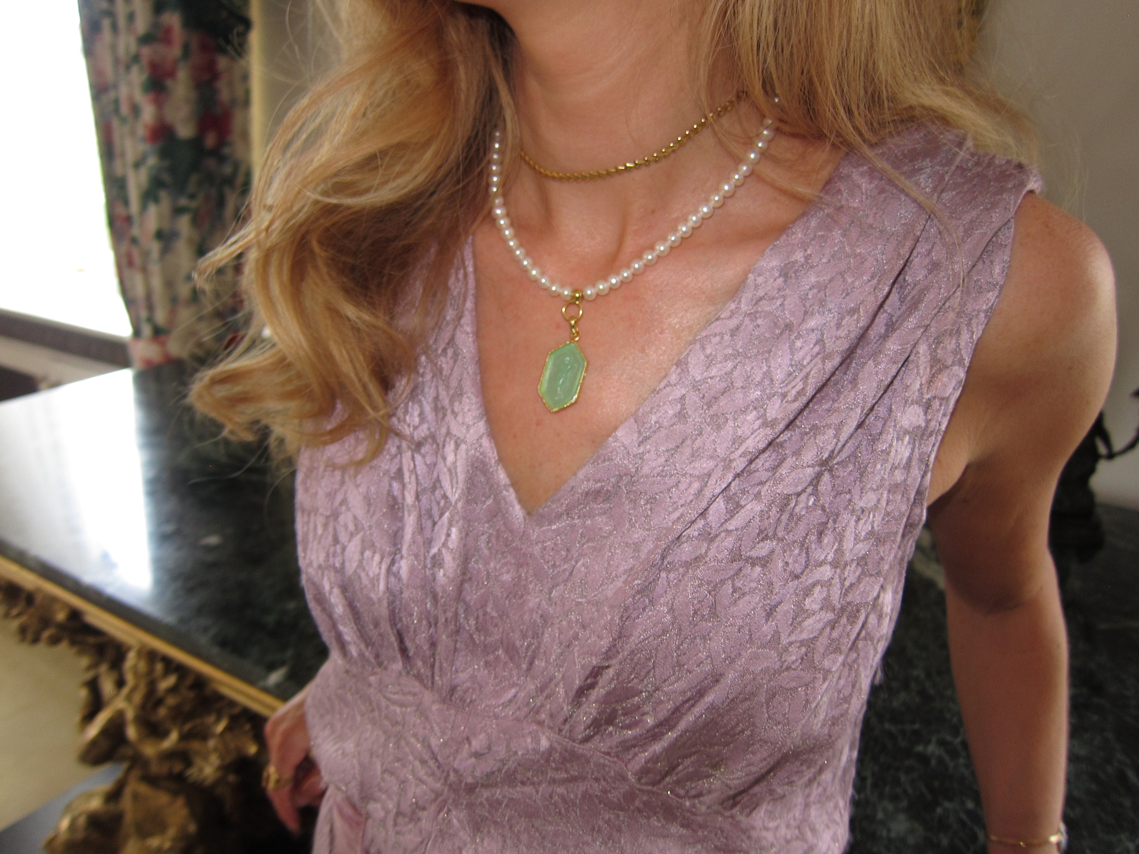 green charm on a pearl necklace a woman wearing it with a lilac dress