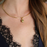 A close-up of a model wearing a delicate gold bangle necklace with a small green  pendant, paired with a black lace top.