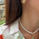 Close-up of a person wearing gold earrings and a pearl necklace with a green pendant.
