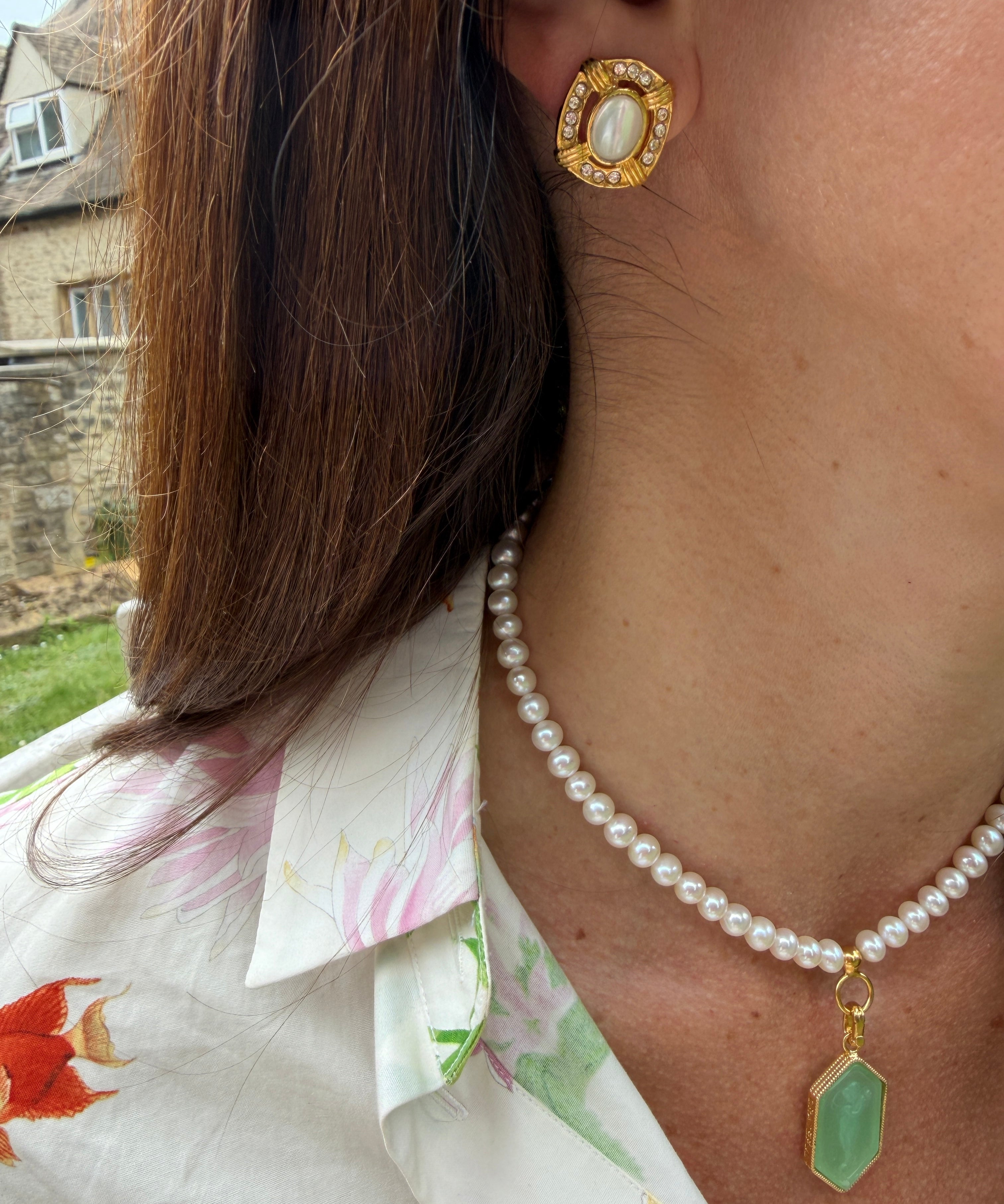Close-up of a person wearing gold earrings and a pearl necklace with a green pendant.