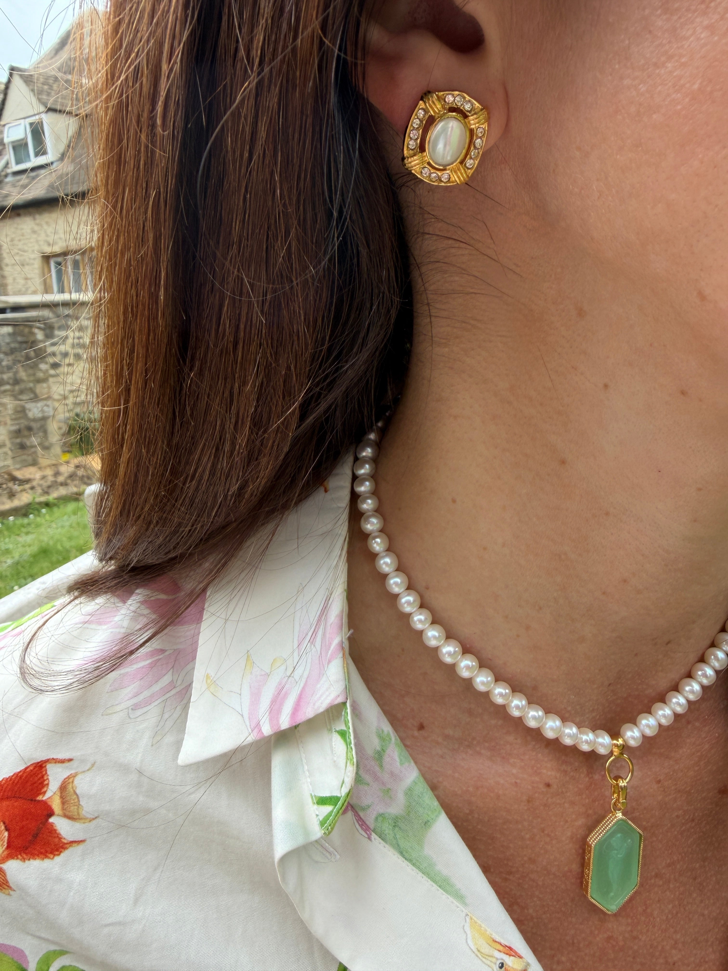 Close-up of a person wearing gold earrings and a pearl necklace with a green pendant.