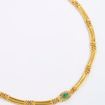A gold-toned necklace with a distinctive segmented, twisted bamboo-like design and a central oval green stone surrounded by small clear stones, shown on a plain white background.