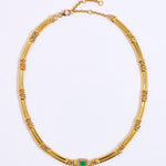 A gold chain necklace with a bamboo-inspired segmented design and a central green emerald accent, surrounded by clear sparkling crystals, displayed on a clean white background.