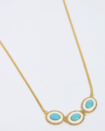 Close-up product shot of a statement necklace with three oval turquoise stones set in glossy white enamel with matching earrings on a white background.