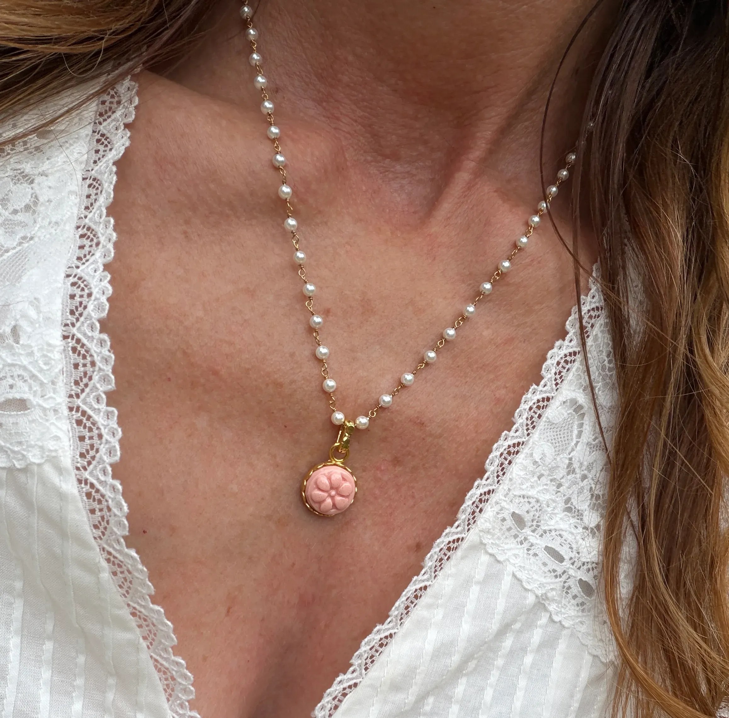 Pearl necklace with a pink pendant worn by a person in a white lace top.