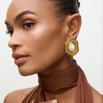 Woman wearing gold earrings with a pearl center on a neutral background