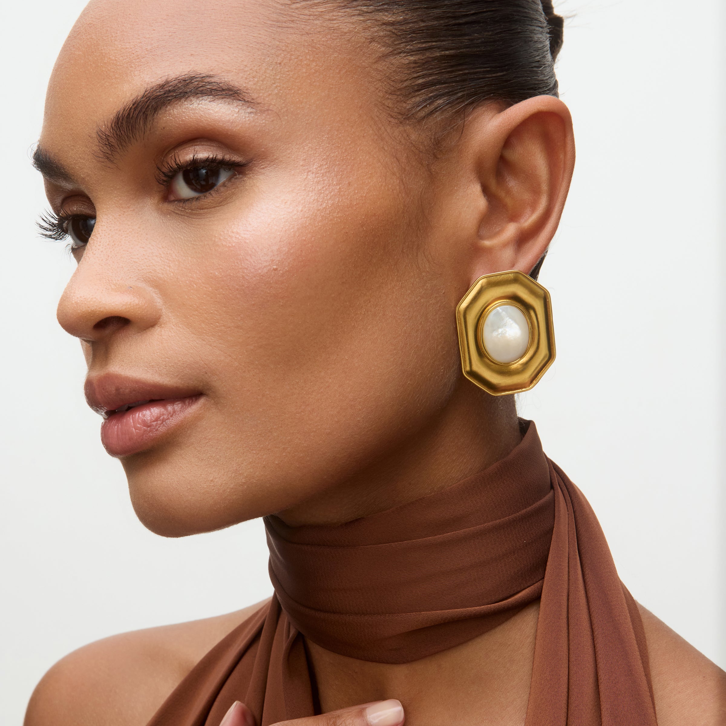 Woman wearing gold earrings with a pearl center on a neutral background