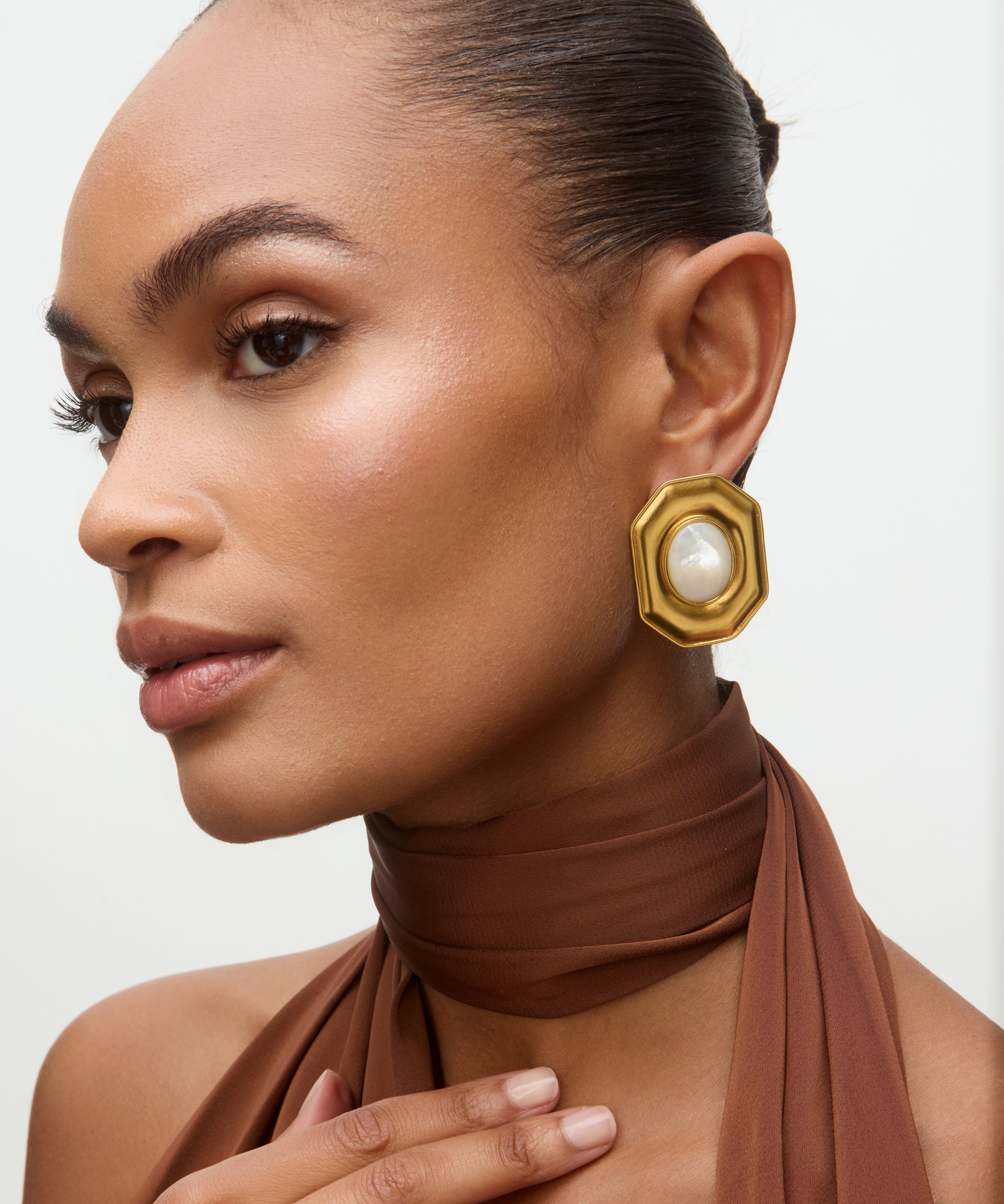Woman wearing gold earrings with a pearl center on a neutral background