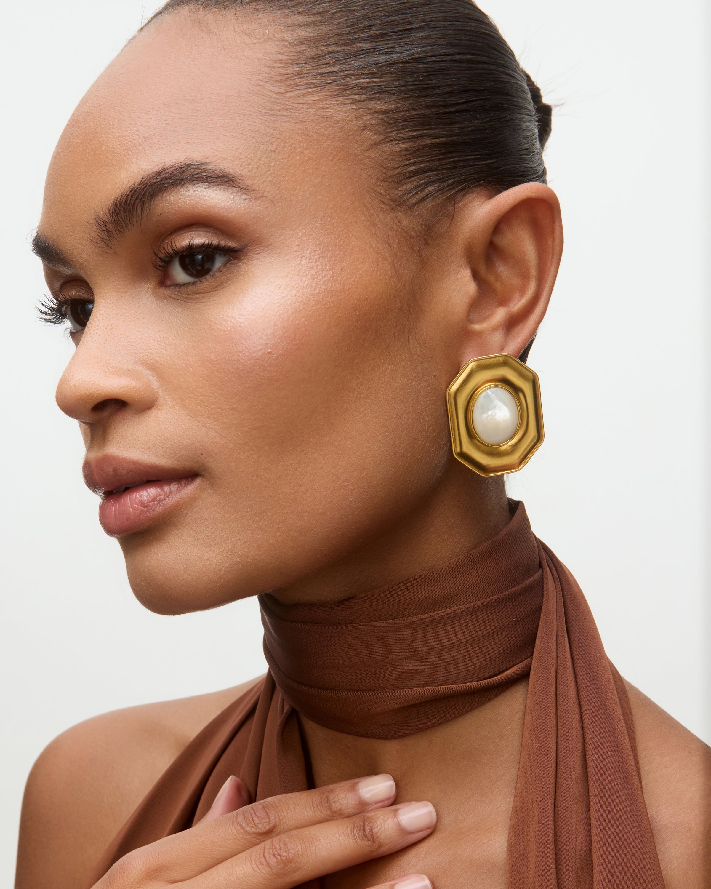 Woman wearing gold earrings with a pearl center on a neutral background