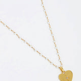 close up image shot of the Soru Jewellery clear crystal surrounded by a star etching set in a shiny gold heart attached to a white beaded necklace on a white background