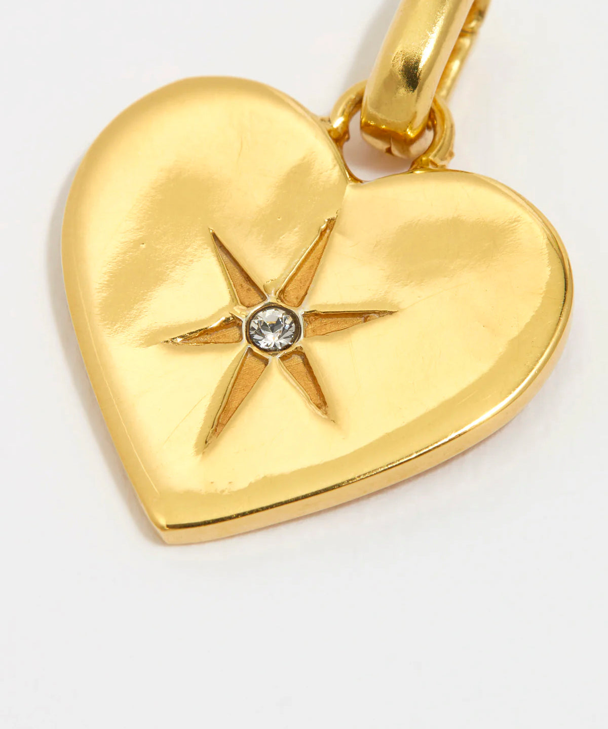 close up image shot of a clear crystal surrounded by a star etching set in a shiny gold heart on a white background