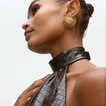 Close-up model image of gold sunburst earrings with rhinestone centres on a white background 