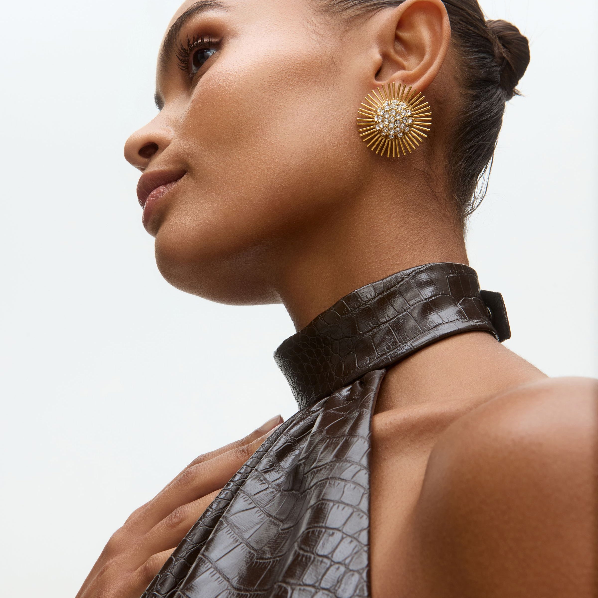 Close-up model image of gold sunburst earrings with rhinestone centres on a white background 