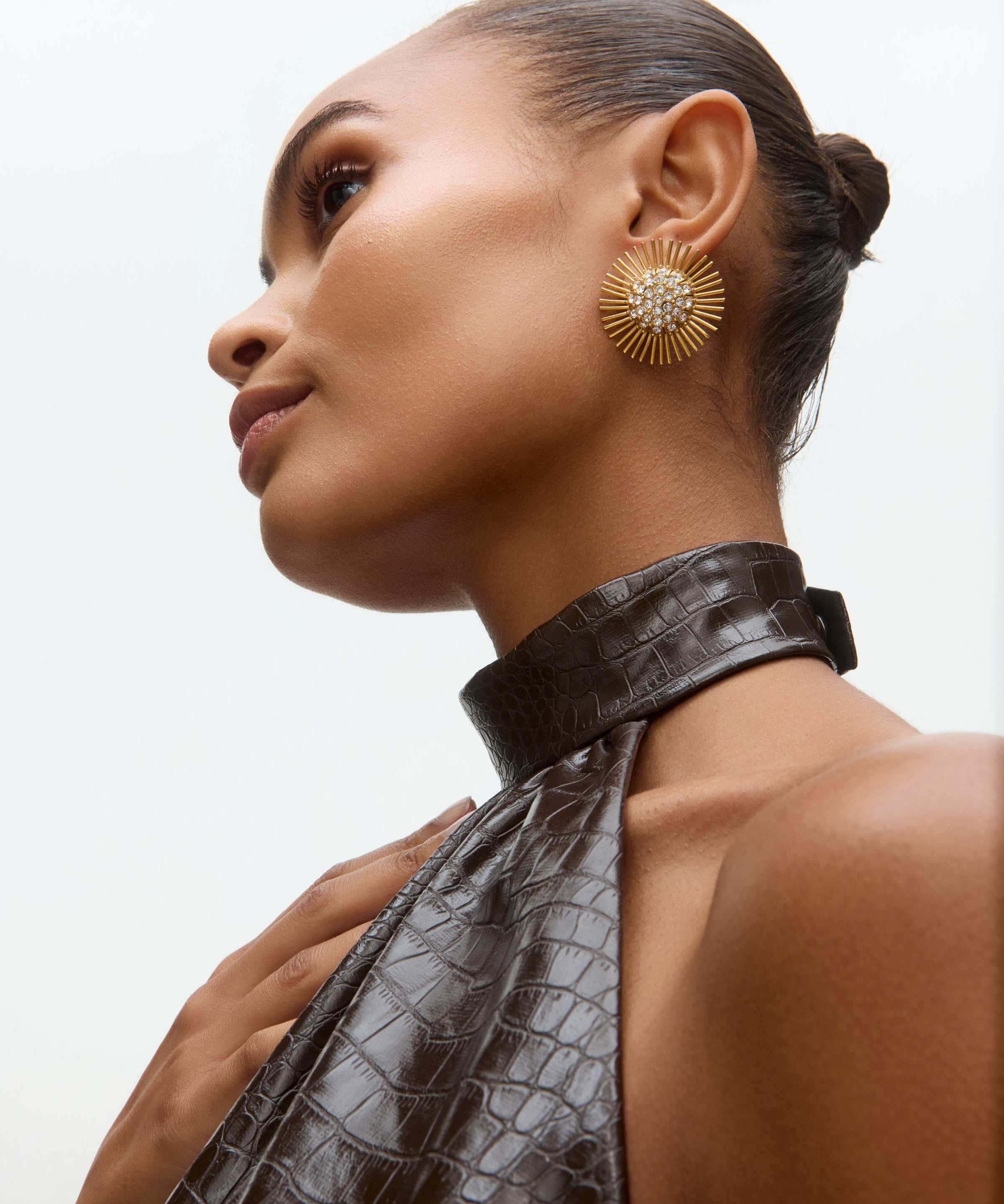 Close-up model image of gold sunburst earrings with rhinestone centres on a white background 
