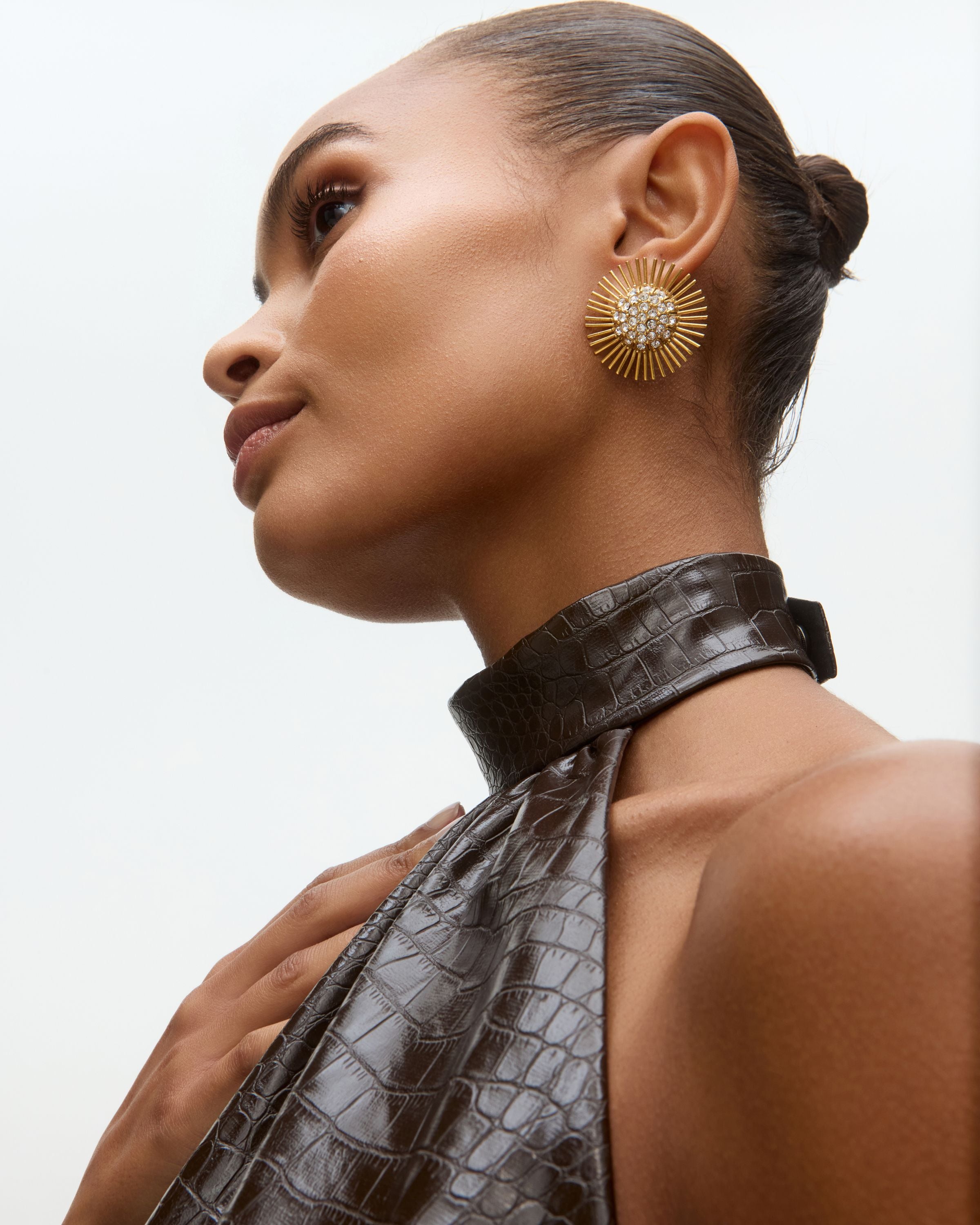 Close-up model image of gold sunburst earrings with rhinestone centres on a white background 
