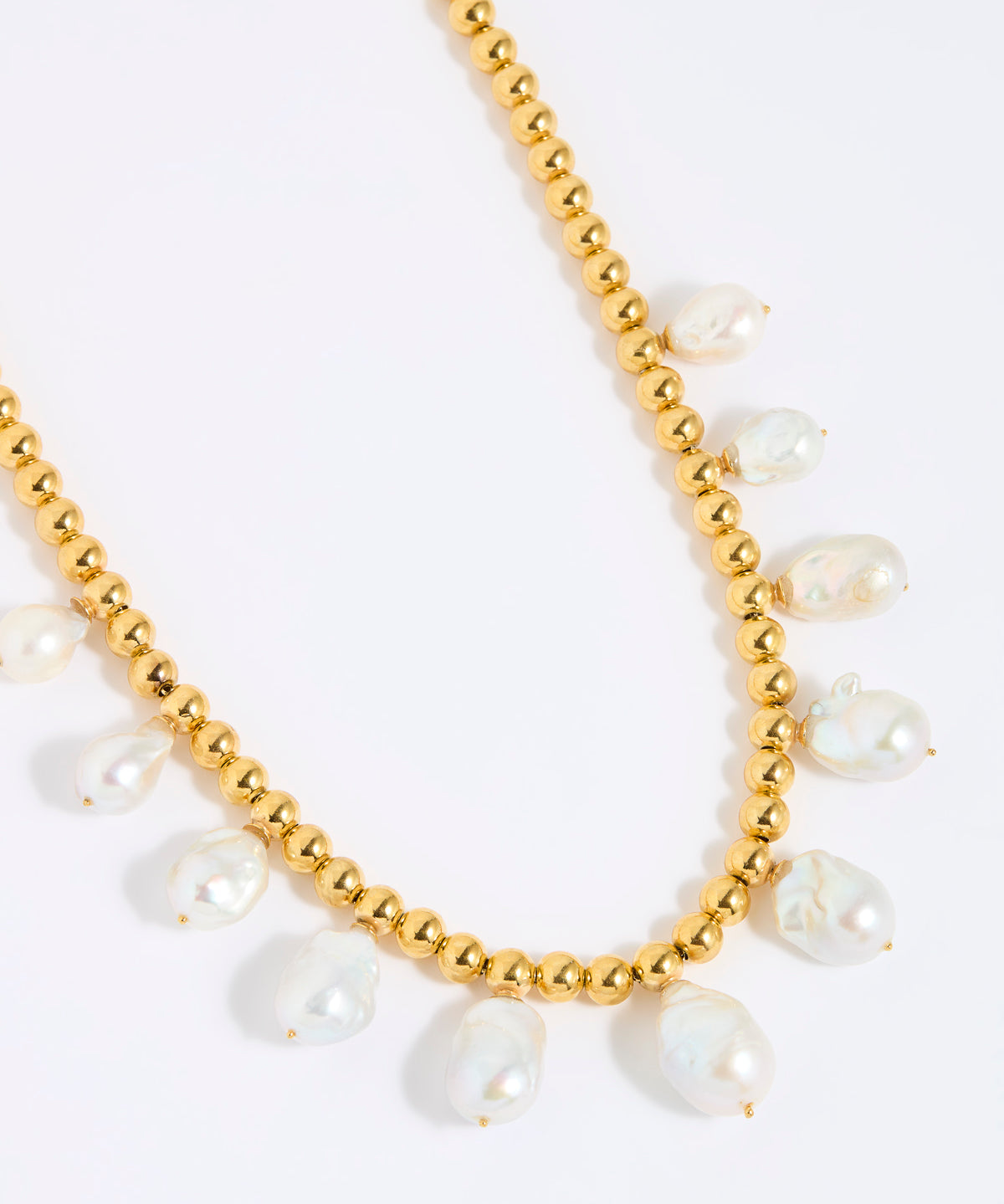 Gold beaded necklace with statement white pearls on a white background