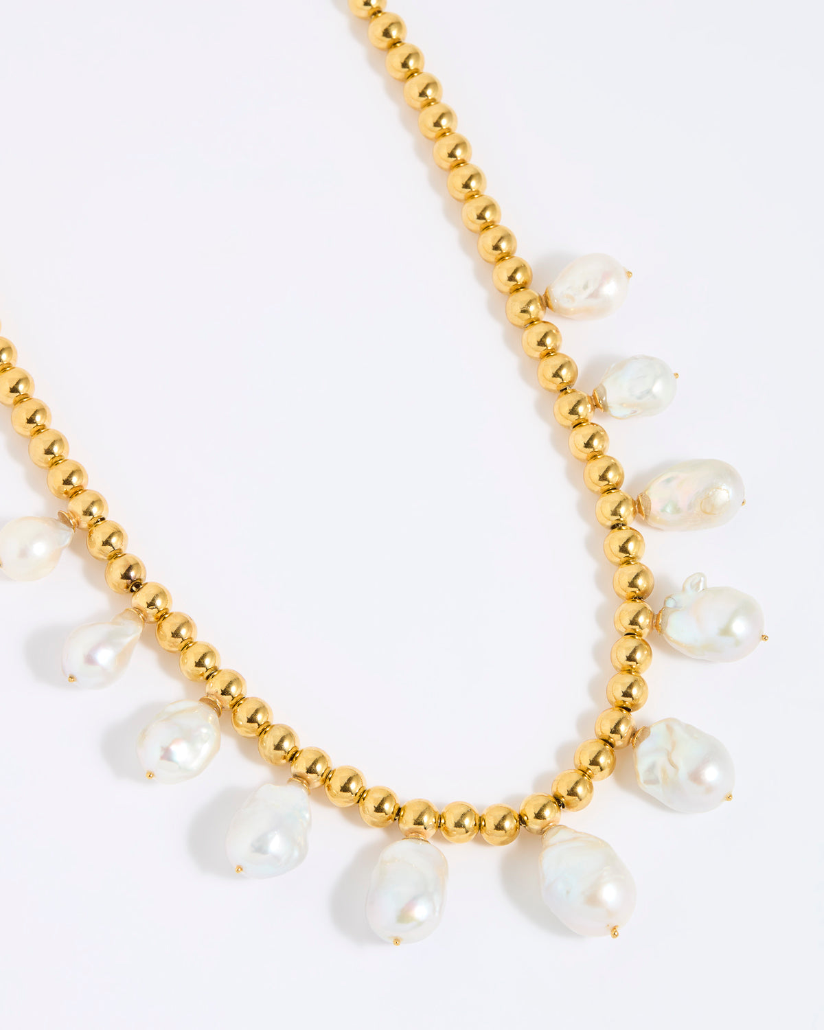 Gold beaded necklace with statement white pearls on a white background