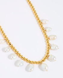 Gold beaded necklace with statement white pearls on a white background