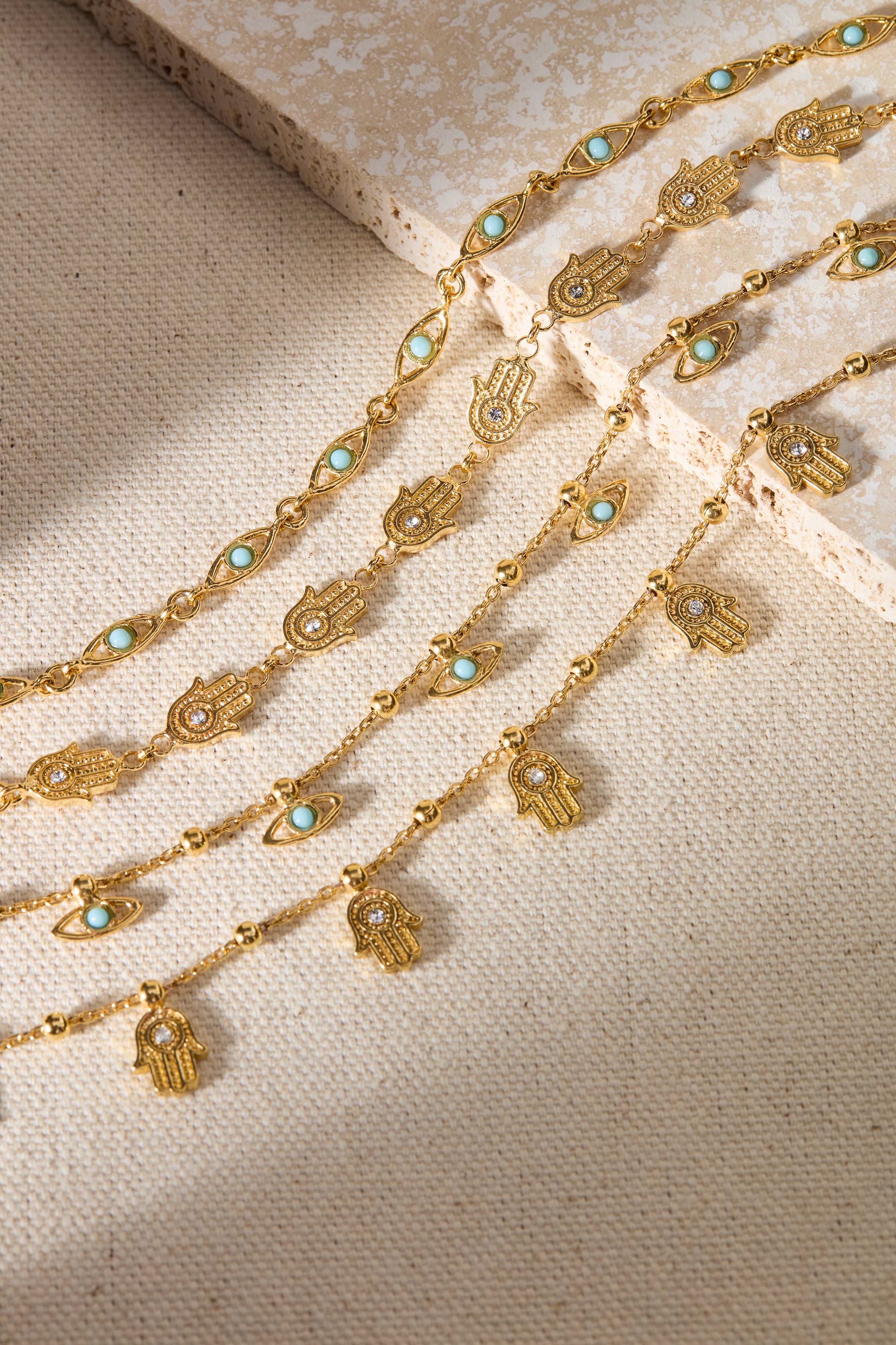 Gold chain necklace with hamsa hand and turquoise stone pendants on a beige fabric background