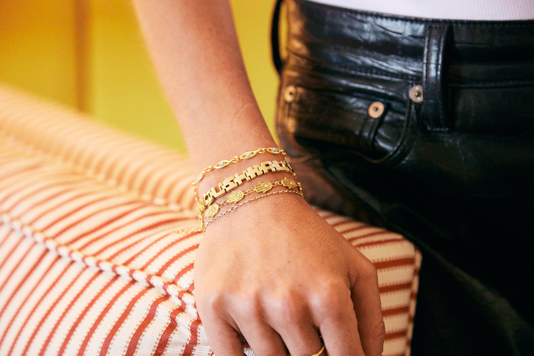 A close-up of a person's hand resting on a striped cushion, wearing a stack of gold bracelets.
