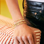A close-up of a person's hand resting on a striped cushion, wearing a stack of gold bracelets.