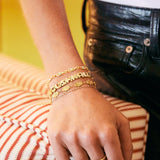 A close-up of a person's hand resting on a striped cushion, wearing a stack of gold bracelets.