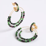 A pair of delicate gold double-hoop earrings, adorned with multiple strands of small, faceted beads in rich shades of green, dark charcoal, and purple, displayed against a white background.