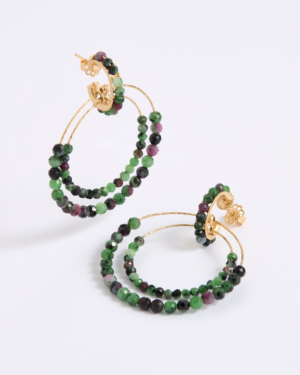 A pair of delicate gold double-hoop earrings, adorned with multiple strands of small, faceted beads in rich shades of green, dark charcoal, and purple, displayed against a white background.