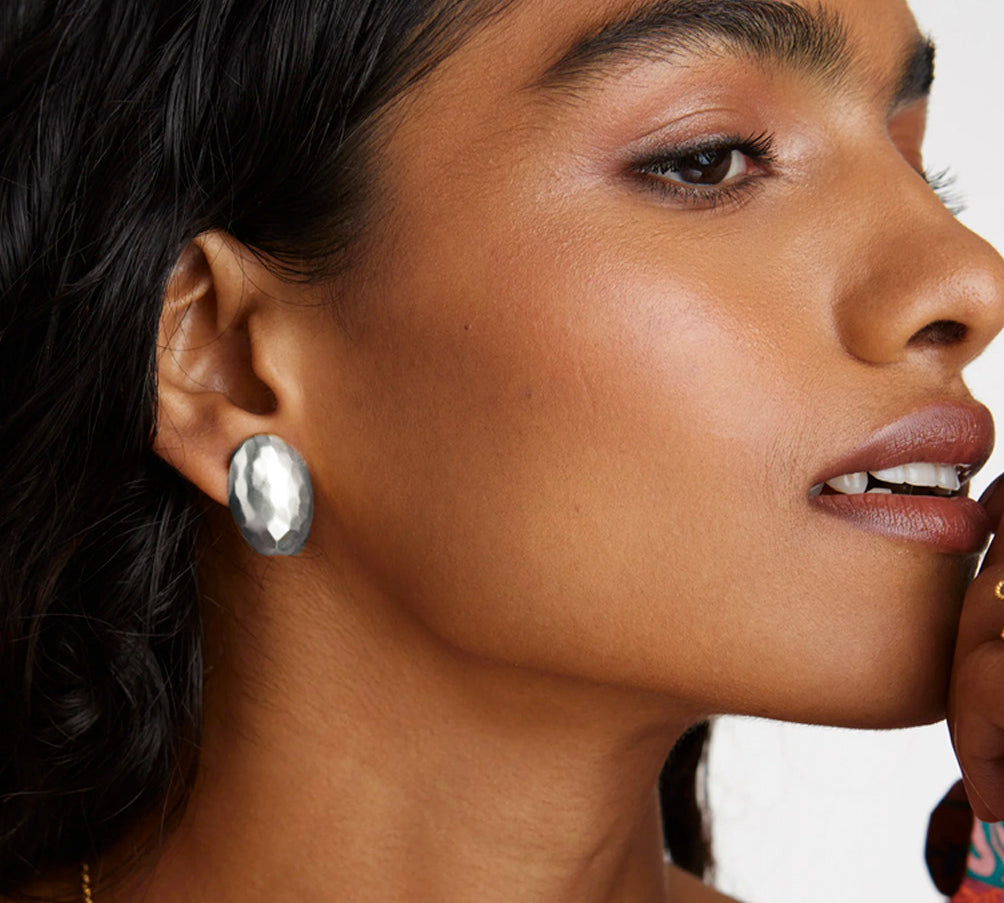 A model shot of a lady wearing modern silver stud earrings, featuring a delicate hammered effect to the surface