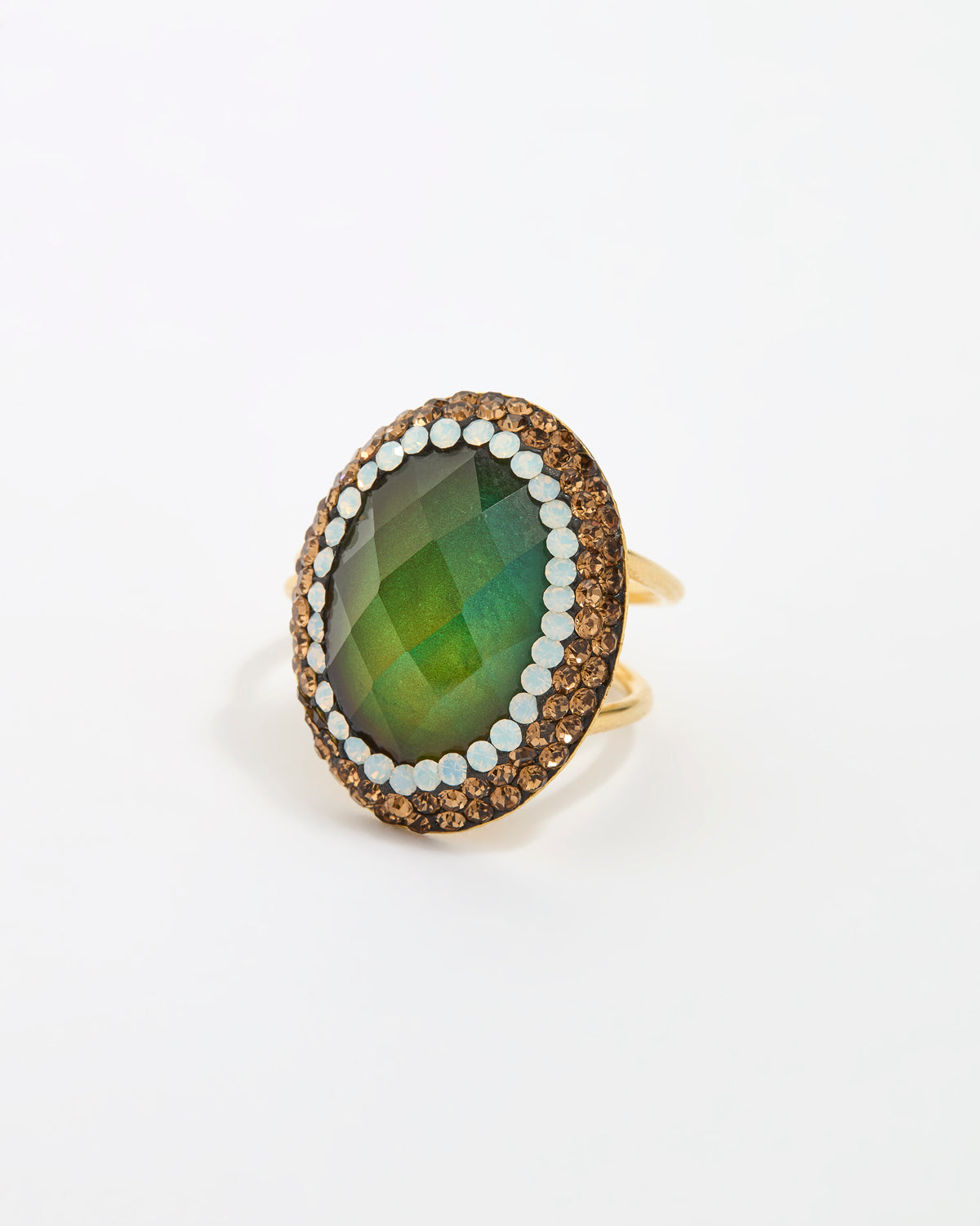 An oval ring featuring a faceted green gemstone, surrounded by a double-layered border of gold and opal stones, set on a polished gold band against a clean, plain white background.
