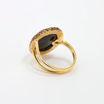 Reverse image of a  gold ring with a large oval dark mood stone centre stone and a halo of small gold stones, photographed on a clean white background.