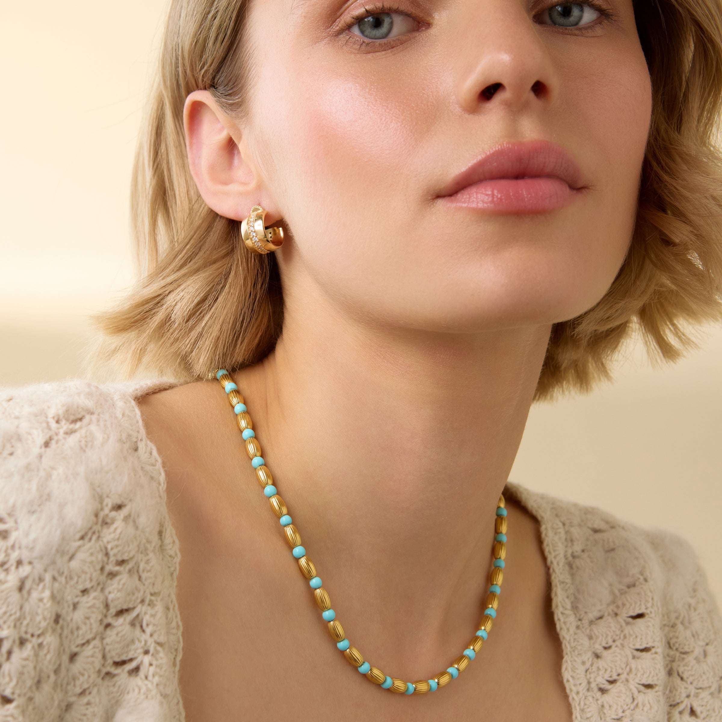 Close-up of a model wearing gold plated silver and turquoise beaded necklace with toggle clasp fastener at the back on a neutral  background.