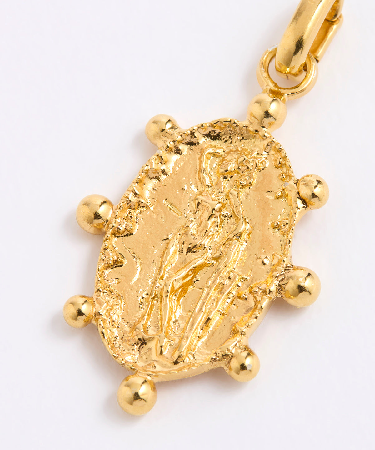 A close-up of a textured gold charm pendant featuring an embossed figure, surrounded by small gold beads, on a plain white background.