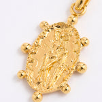 A close-up of a textured gold charm pendant featuring an embossed figure, surrounded by small gold beads, on a plain white background.