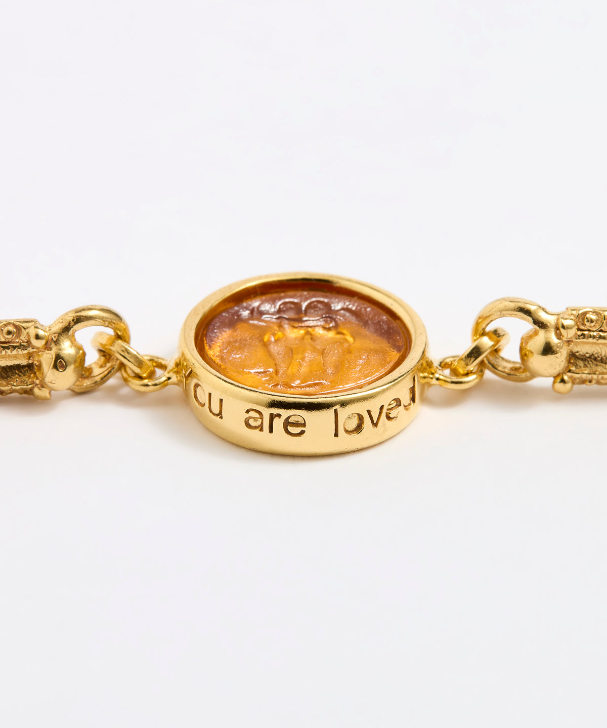 Close up of Gold link bracelet with round pendant in the centre with amber  glass and inscription 'you are loved ' 