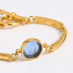 Close up Gold link bracelet with round pendant in the centre with blue glass 
