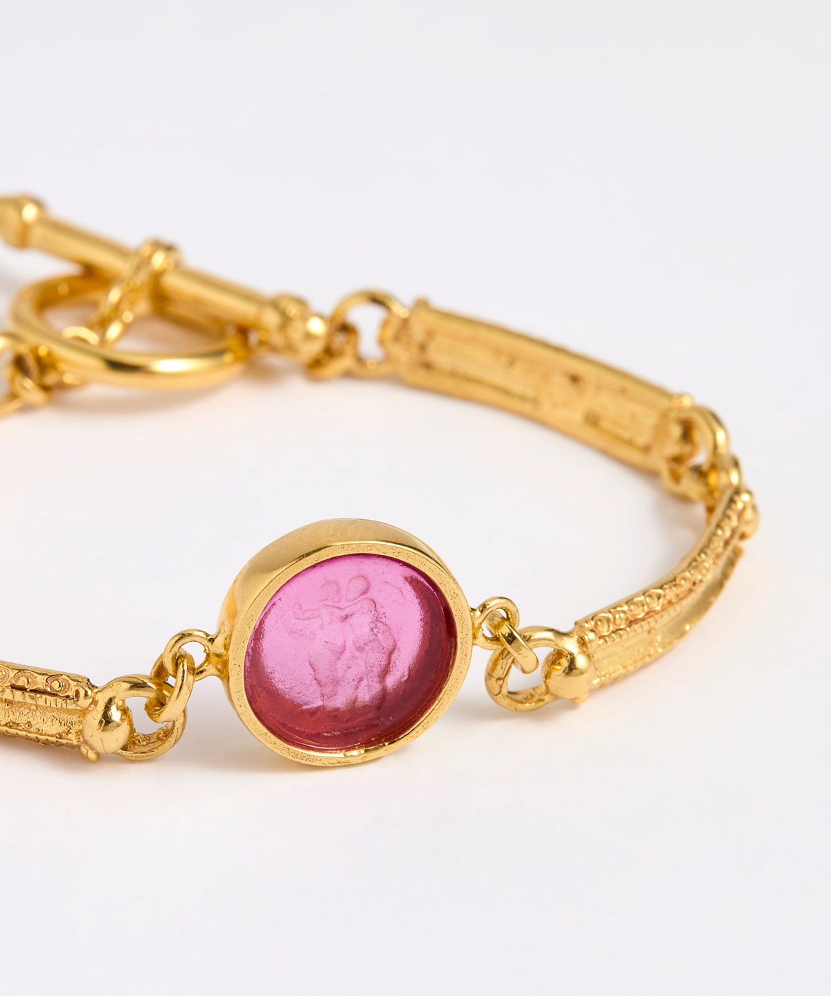 Close up Gold link bracelet with round pendant in the centre with magenta glass