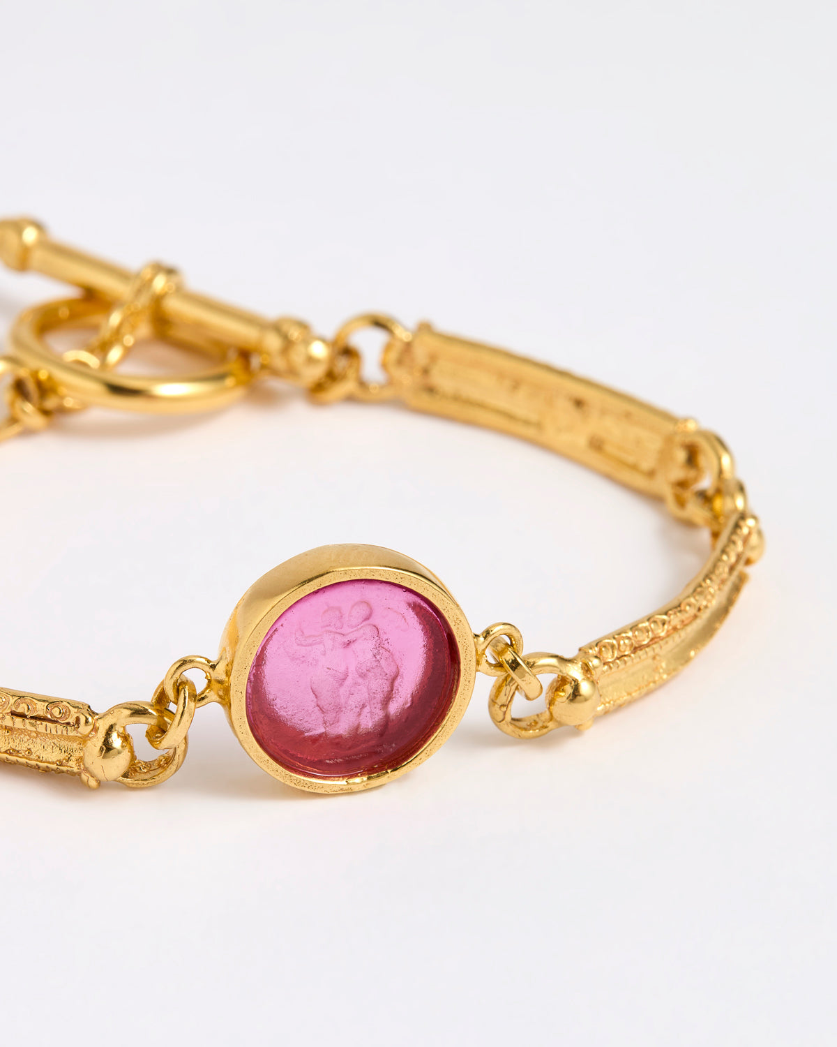 Close up Gold link bracelet with round pendant in the centre with magenta glass