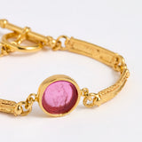 Close up Gold link bracelet with round pendant in the centre with magenta glass
